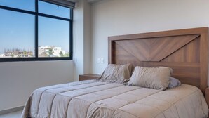 Ein Schlafzimmer mit großem Fenster, einem Holzkopfende und einer beigen Bettdecke.