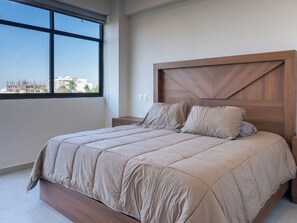 Ein Schlafzimmer mit großem Fenster, einem Holzkopfende und einer beigen Bettdecke.