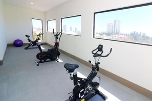 Ein Fitnessraum mit Ergometer und einem violetten Trainingsball, große Fenster mit Blick auf die Stadt.