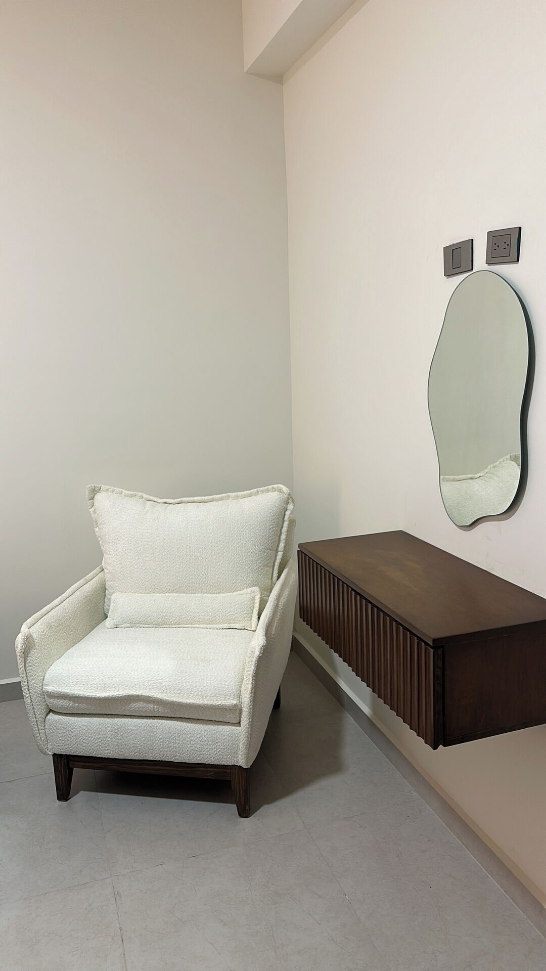 Une pièce comprenant un fauteuil blanc, une console en bois et un miroir fixé au mur.