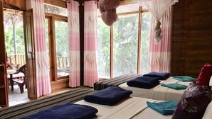 Ein Zimmer mit zwei Betten, jedes mit einem blauen Kopfkissen und einem grünen Handtuch, und Blick ins Freie durch große Fenster.