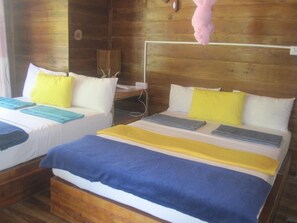 Dos camas con ropa de cama blanca y azul, almohadas amarillas y un cabecero de madera.