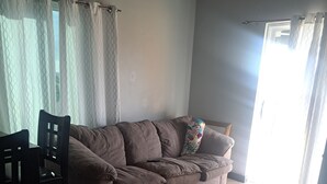 A living room with a brown sofa, a wooden dining table with chairs, and a window with curtains. - Stylish apartment close to attractions, dining, shopping, and entertainment (Montego Bay)