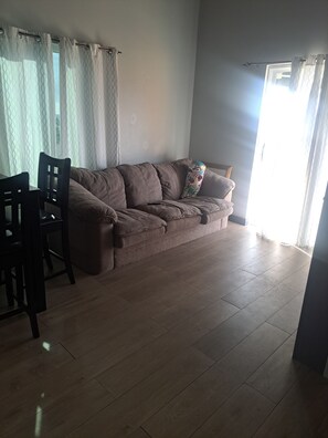 A living room with a brown sofa, a wooden dining table with chairs, and a window with curtains. - Stylish apartment close to attractions, dining, shopping, and entertainment (Montego Bay)