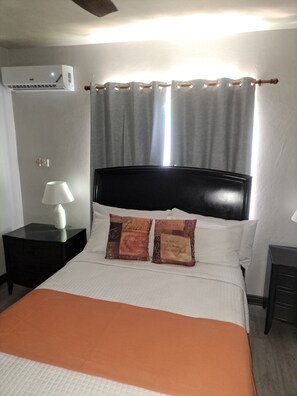 Ein Hotelzimmer mit Bett, Nachttisch mit Lampe, Wandaircondition und einem Vorhangfenster.