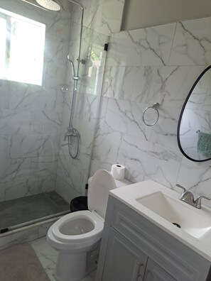 A bathroom with a shower, toilet, sink, and marble walls. - Stylish apartment close to attractions, dining, shopping, and entertainment (Montego Bay)