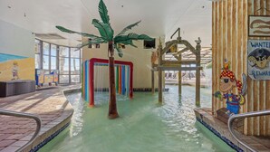 Parque acuático interior con piscina, una palmera y un mural.