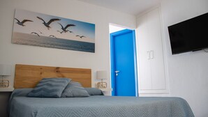 A bedroom with a bed, a blue door, a wall-mounted TV, and a painting of birds. - Front line beach penthouse with large terrace facing the sea! (Puerto de la Cruz)