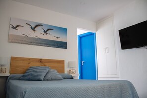 Un dormitorio con cama, una puerta azul, un televisor y un cuadro de pájaros.