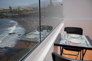 Un balcón con mesa lista para comer, con vista a una playa con gente y sombrillas.