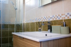 Un baño con ducha, lavamanos con espejo y salpicadero de azulejos.