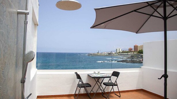 A balcony with a table and chairs, a shower, and a view of the sea and buildings. - Front line beach penthouse with large terrace facing the sea! (Puerto de la Cruz)