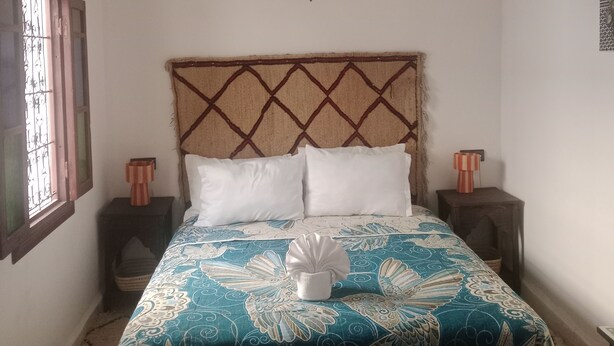 A bed with a patterned bedspread, two pillows, a decorative wall hanging, and a ceiling light fixture.