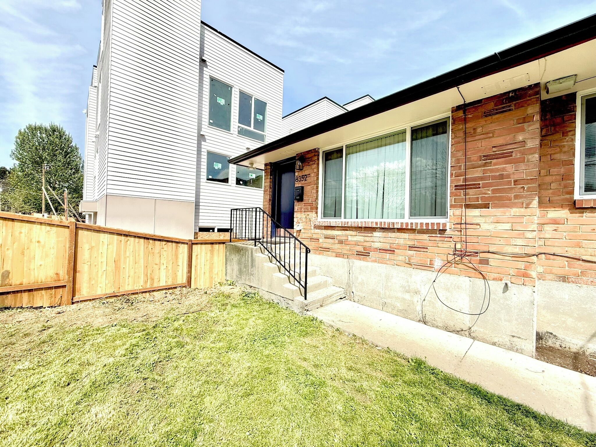 A residential building with a brick facade, a wooden fence, and a grassy yard.