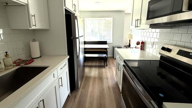 Una cocina moderna con armarios blancos, una estufa negra y un ventanal que proporciona luz natural.