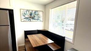 Cocina compacta con una banca integrada, un refrigerador de acero inoxidable y una ventana con persianas.