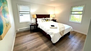 Un dormitorio con cama, dos mesitas de noche, una lámpara de techo y dos ventanas con persianas.
