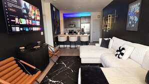 Een moderne woonkamer met een flatscreentelevisie, een plafondventilator, een bank, een salontafel en een keuken in de achtergrond.