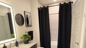 Een moderne badkamer met een wastafel, toilet en douchegedeelte, met een zwart douchegordijn en een potplant op het aanrecht.