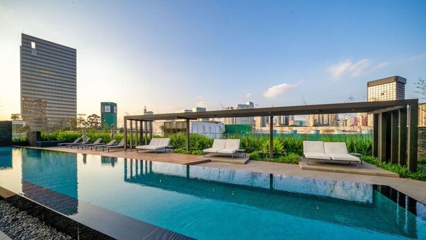 A rooftop pool with lounge chairs, a pergola, and city buildings in the background. - Studio Espaçoso - Pinheiros (São Paulo)