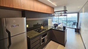 A modern kitchen with a built-in oven, a refrigerator, and a large window offering a city view. - Studio Espaçoso - Pinheiros (São Paulo)