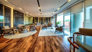 A spacious lounge area with wooden flooring, multiple seating arrangements, and large windows offering views of the city. - Studio Espaçoso - Pinheiros (São Paulo)