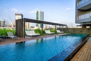 Une piscine sur le toit, dotée de chaises longues, d’une pergola et offrant une vue sur la ville.