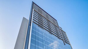 A modern high-rise building with reflective glass facade, large windows, and a prominent entrance with a landscaped area in front. - Studio Espaçoso - Pinheiros (São Paulo)