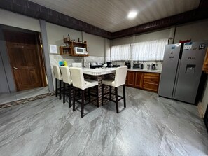 A kitchen with a dining table, chairs, a refrigerator, and a microwave. - Casa Del Sol: Privacy, comfort and unforgettable moments. (Provincia de Guanacaste)