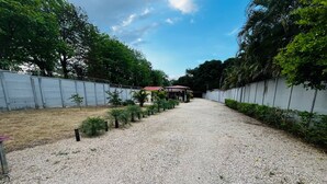Un chemin de gravier mène à un bâtiment doté d’un toit rouge, entouré de verdure et d’une clôture en métal.