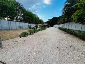 A gravel pathway leading to a building with a red roof, surrounded by greenery and a metal fence. - Casa Del Sol: Privacy, comfort and unforgettable moments. (Provincia de Guanacaste)