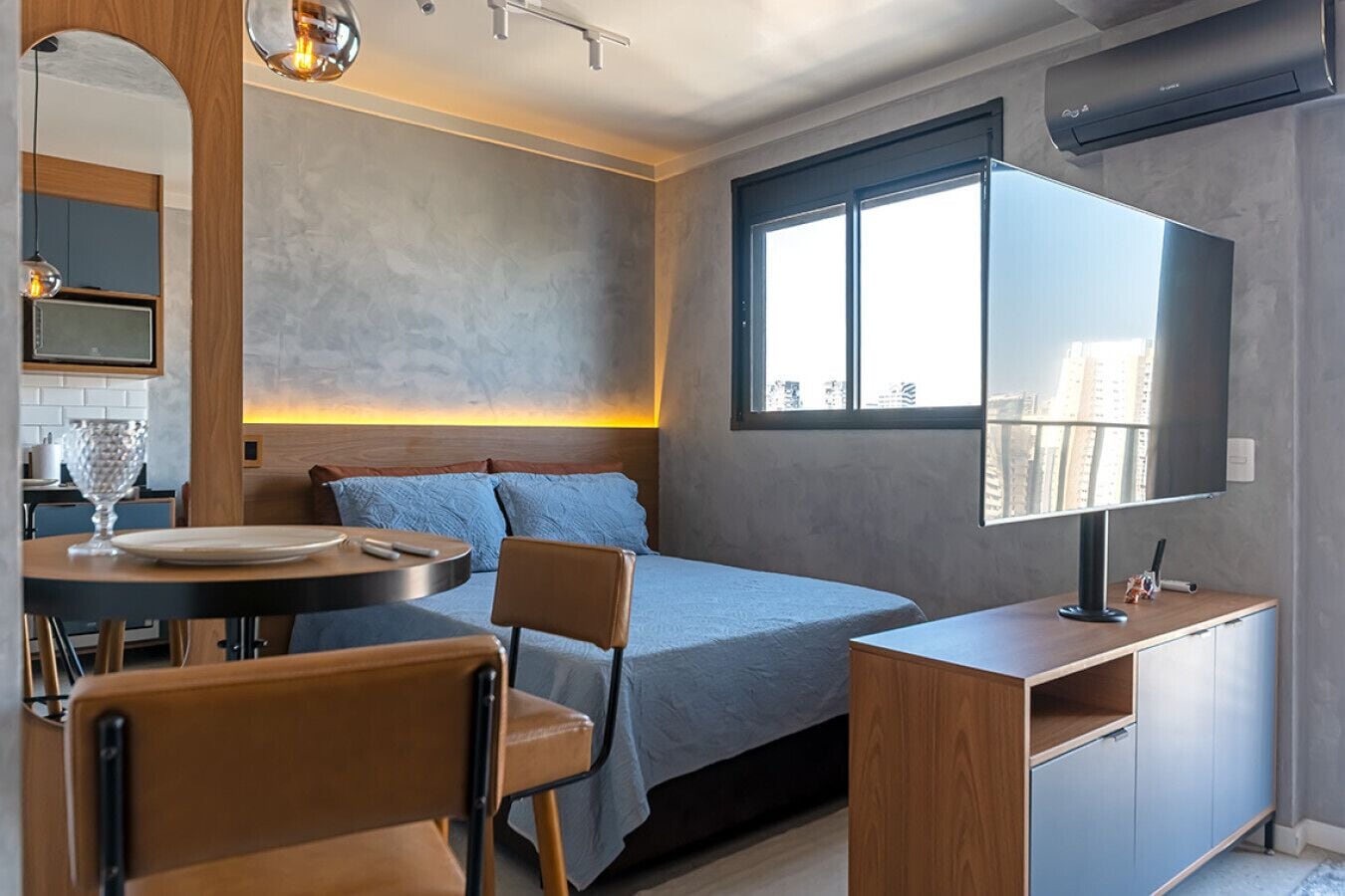 Une chambre moderne avec un lit, une table de chevet, une télévision et une fenêtre donnant sur la ville.