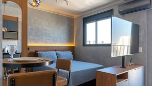 Una camera da letto moderna con un letto, un comodino, una TV e una finestra vista città.
