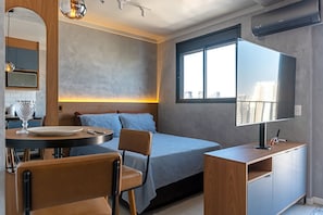 Ein modernes Schlafzimmer mit Bett, Nachttisch, Fernseher und einem Fenster mit Blick auf die Stadt.