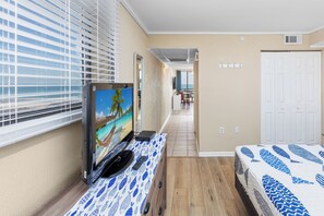 Ein Hotelzimmer mit Fernseher, einem Bett mit gemustertem Überwurf, Holzboden, Fenster mit Jalousien und einer Tür.