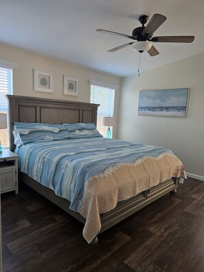 A bedroom with a bed, a ceiling fan, a nightstand, a lamp, and a painting on the wall.