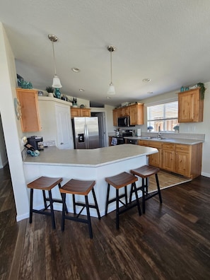 A modern kitchen with a central island, wooden cabinets, stainless steel appliances, and a bar stool seating area.
