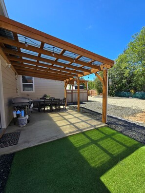 A covered patio with a grill, outdoor seating, and a lawn.