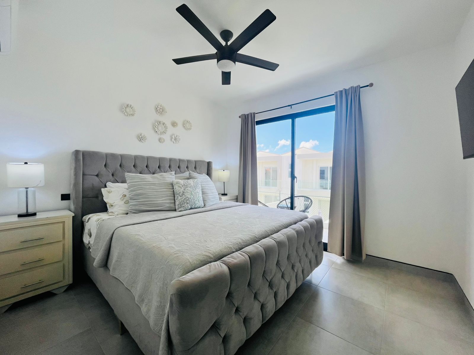 A bedroom with a bed, nightstands, a ceiling fan, and a view through a window.