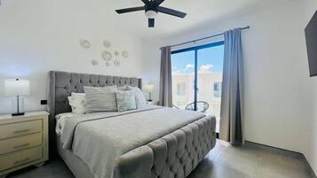 A bedroom with a bed, nightstands, a ceiling fan, and a view through a window.