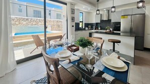 A modern kitchen with a large island, a dining area with a glass table, and a view of a swimming pool. - 3-bedroom house in tranquil Punta Cana with cool AC breeze (Punta Cana)