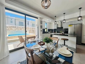 Een moderne keuken met een vastgezet eiland, roestvrijstalen apparatuur en een eethoek met een glazen tafel en stoelen.