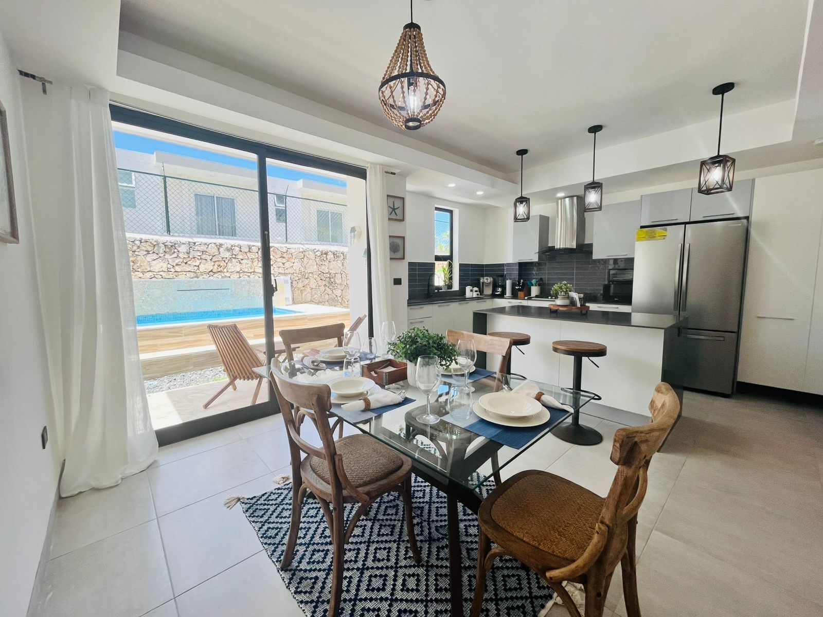 A modern kitchen with a dining area, a pool view, and a stone wall.