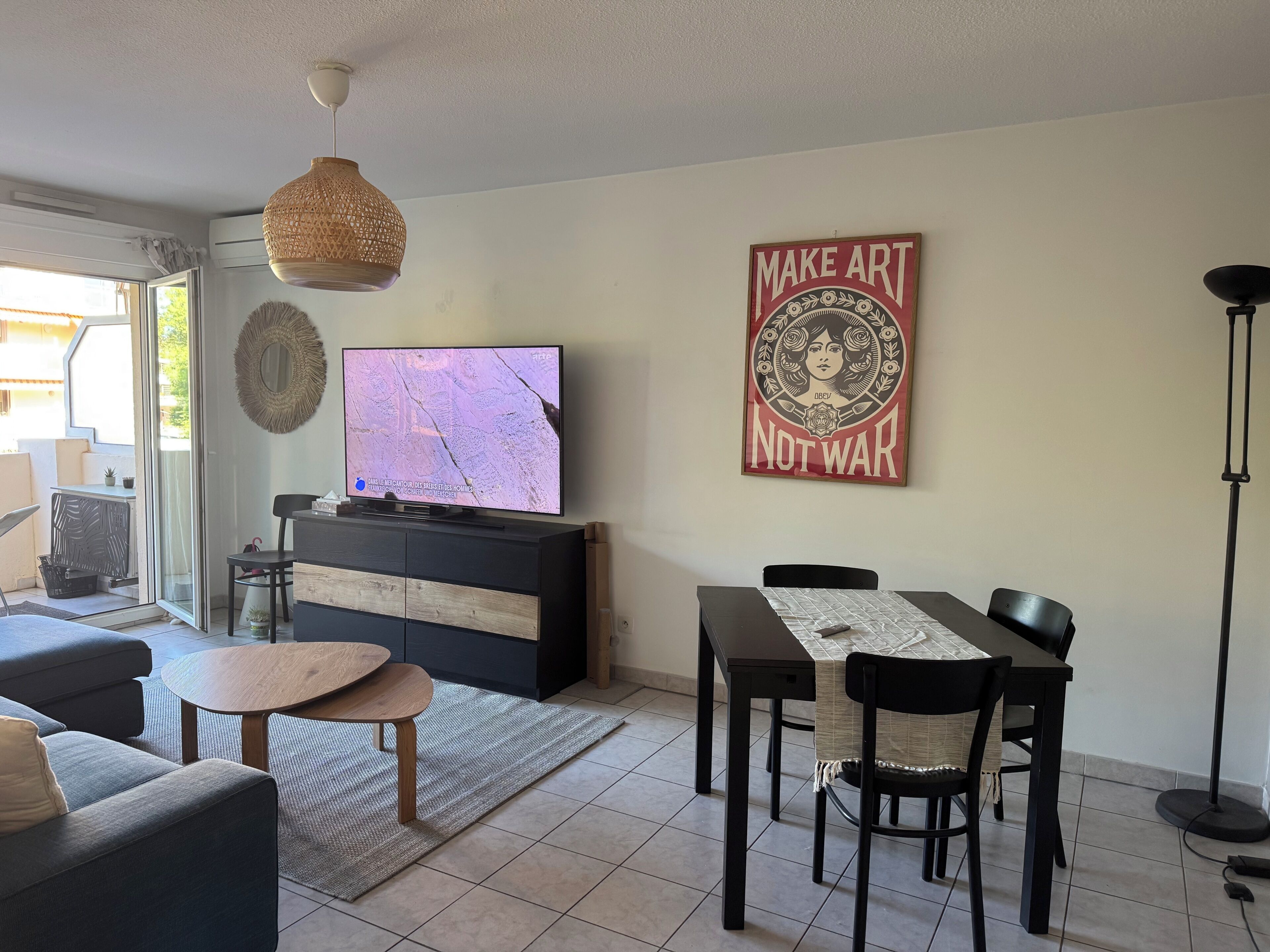 A living room with a TV, a dining table, chairs, a sofa, a floor lamp, and a wall with a poster.