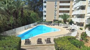 A swimming pool surrounded by a fence, with a multi-story building in the background. - Comfortable central apartment, swimming pool, air conditioning, terrace, parking (Hyères)