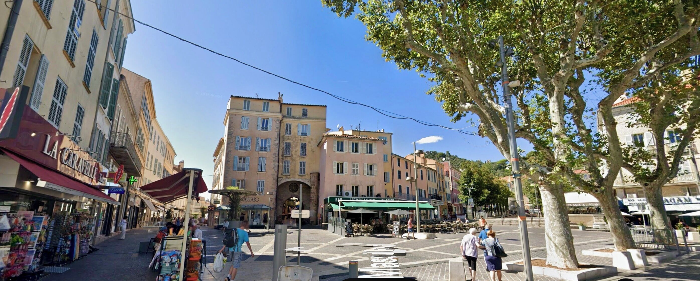 Una calle con tiendas, un café y un edificio con toldo verde.