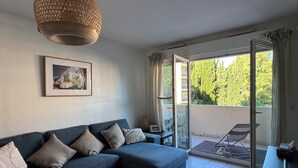 A modern living room with a blue sofa, a wicker lamp, a framed picture, and a sliding glass door leading to an outdoor area. - Comfortable central apartment, swimming pool, air conditioning, terrace, parking (Hyères)