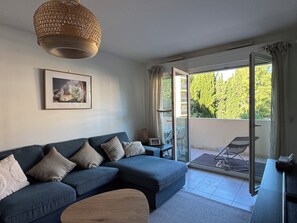 Ein modernes Wohnzimmer mit einem blauen Sofa, einer Korbtaschelampe, einem gerahmten Bild und einer Glastür zum Außenbereich.