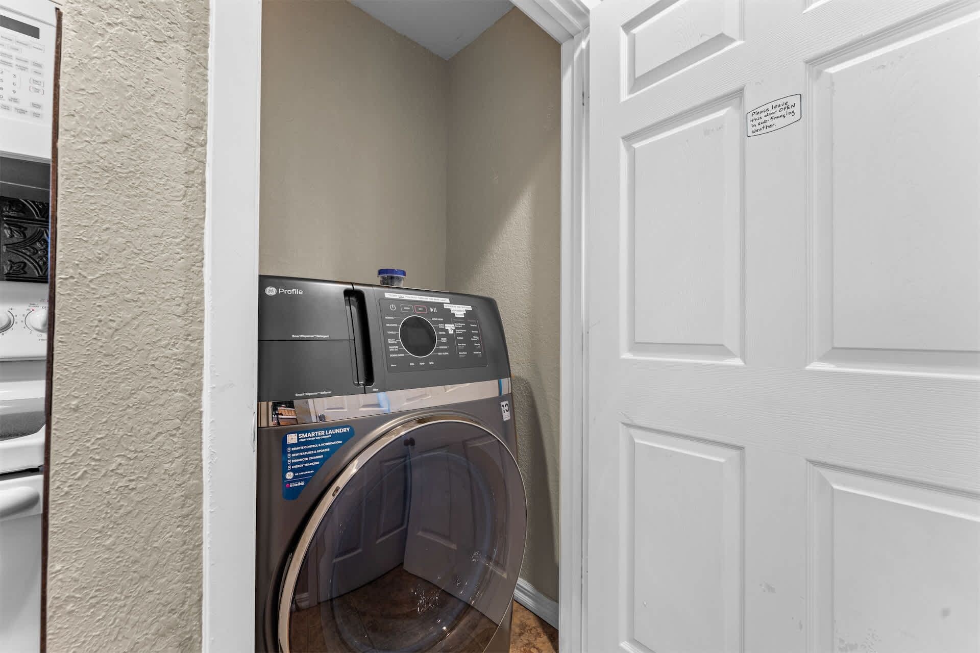 Een kleine wasruimte met een voorlader wasmachine en droger, een deur met een bordje, en een gestructureerde wand.