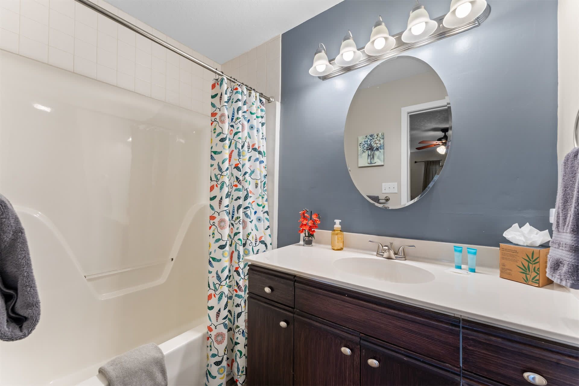 Une salle de bain avec une baignoire, un rideau de douche à motifs floraux, un meuble-lavabo avec un miroir et un porte-serviettes.